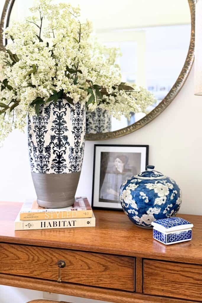 large blue and white vase filled with fluffy white flowers and other decor on a foyer table
