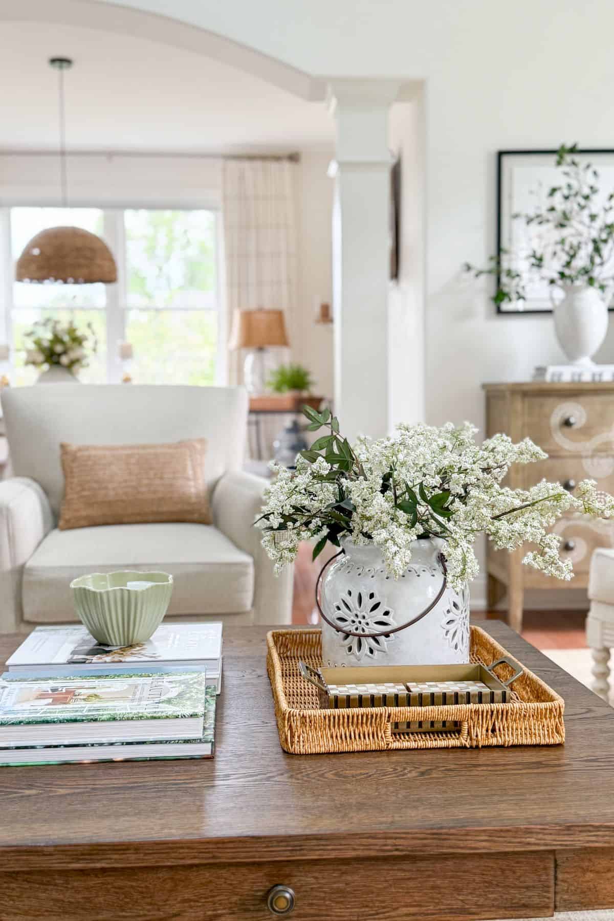 Semi open concept living room with arched doorway, wicker tray, and white ceramic pitcher filled with flowers