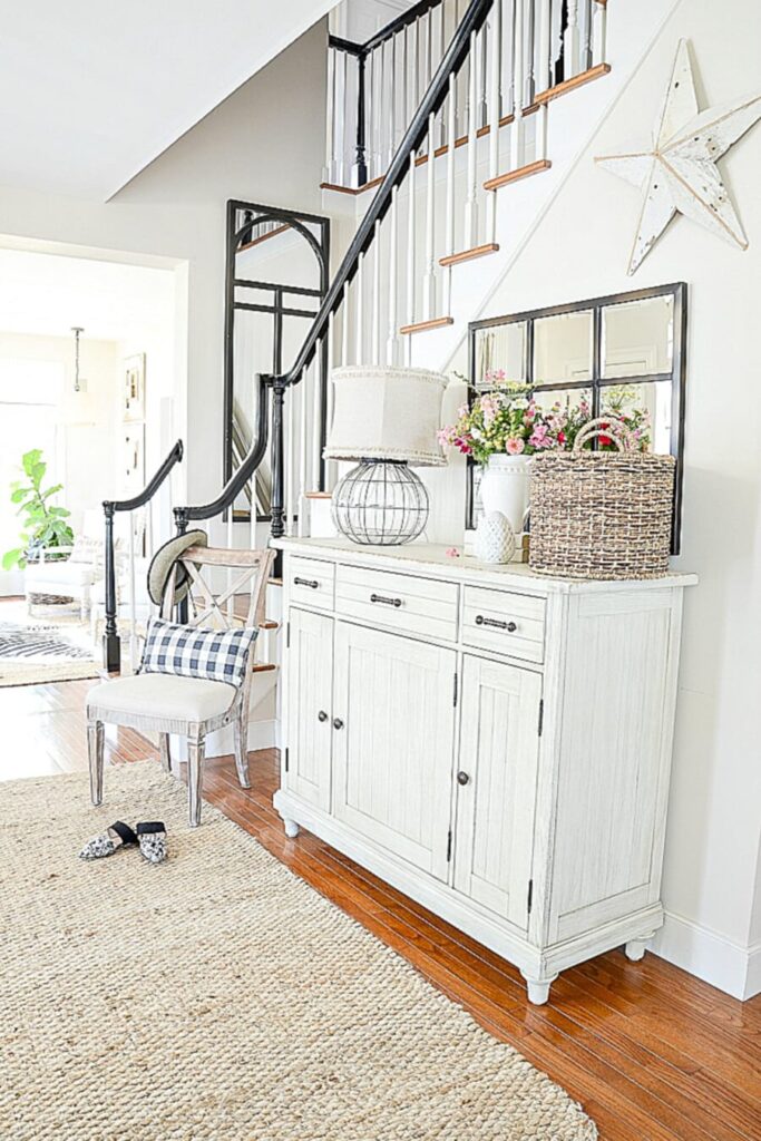 StoneGable foyer with Benjamin Moore Sonnet beige walls, white sideboard, black staircase, and jute rug