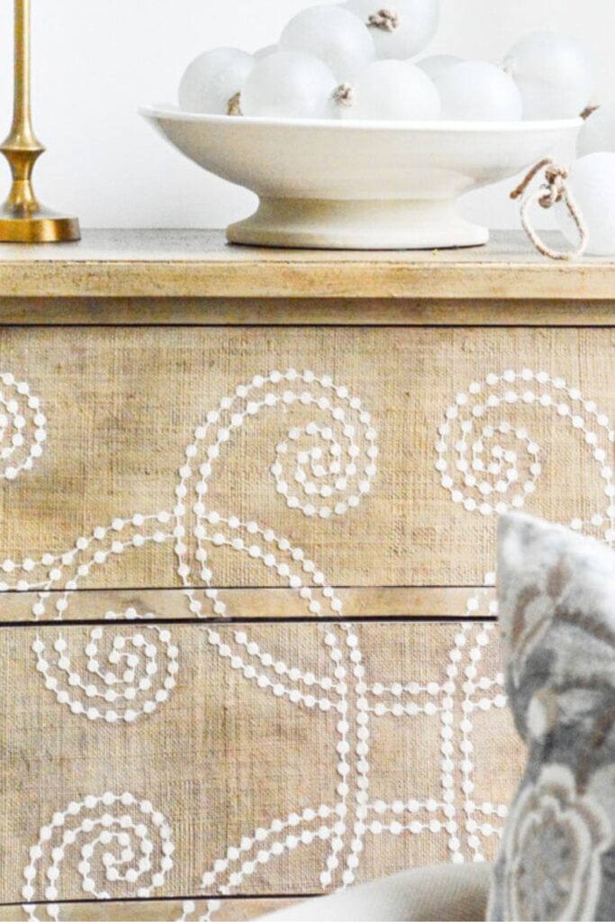 Woven beige dresser with warm undertones styled with a blue and white ginger jar lamp and greenery