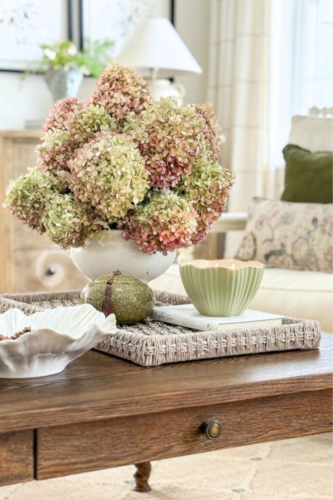 Beige and cream living room styled with dried pink and green hydrangeas, a woven tray, and warm wood coffee table