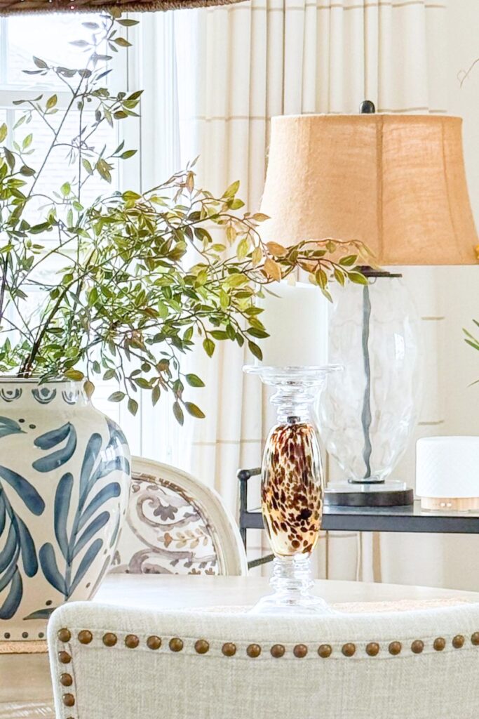 Beige dining nook with a blue and white ginger jar planter, tortoiseshell candlestick, and warm amber lamp shade