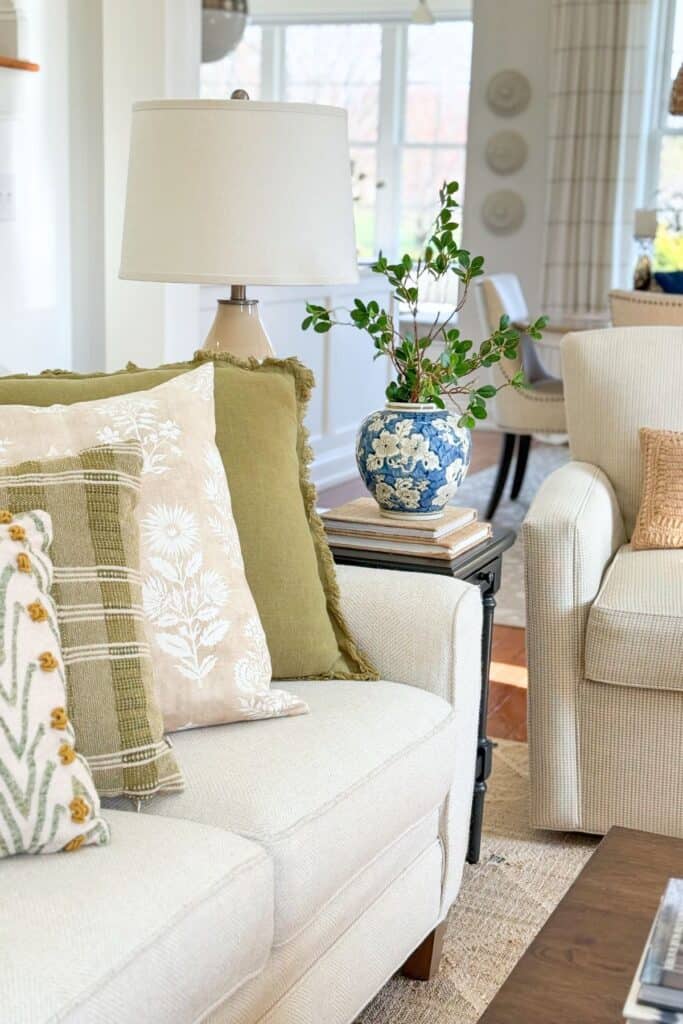 Beige herringbone sofa styled with olive green and cream pillows and a blue and white floral ginger jar