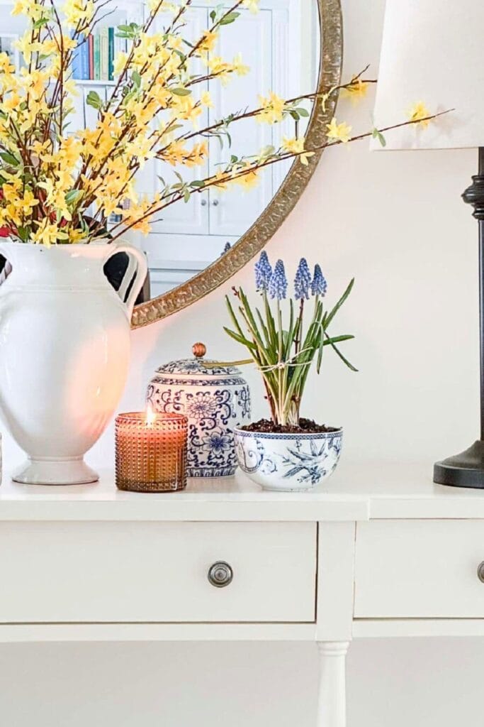 Realistic faux forsythia branches arranged in a white urn on a styled console table