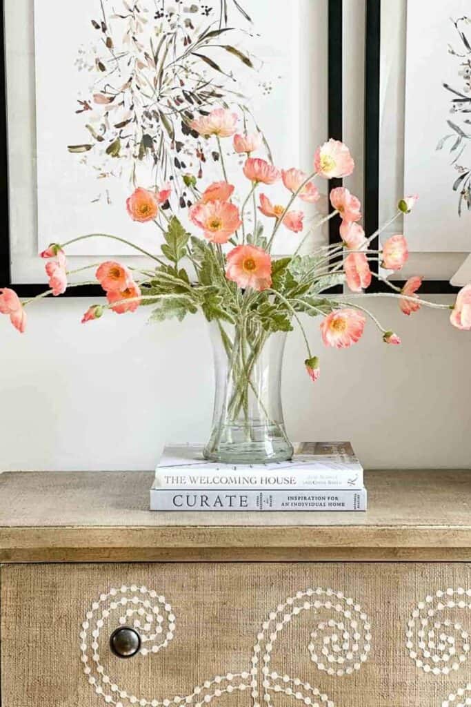 Realistic faux poppies arranged in a clear glass vase with water styled on stacked decorating books