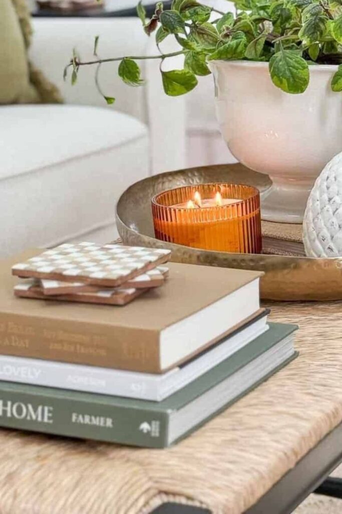 Coffee table styled with tan and green books, an amber candle, jute textures, and a cream urn showing warm beige tones