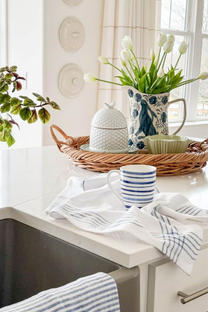 kitchen island styled with woven tray, white tulips, striped mug, and blue and white kitchen towels