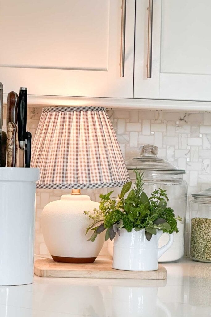 small lamp on kitchen counter styled with fresh herbs and glass canisters