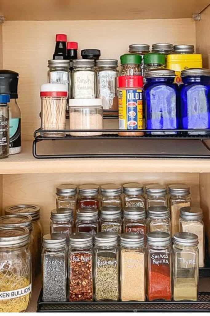 organized kitchen cabinet with tiered spice rack, labeled jars, and pantry staples
