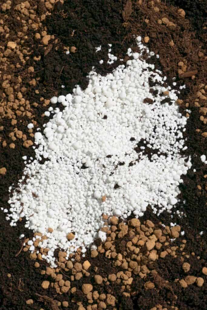 overhead close up view of white perlite and slow release fertilizer granules mixed into rich dark potting soil for container gardening