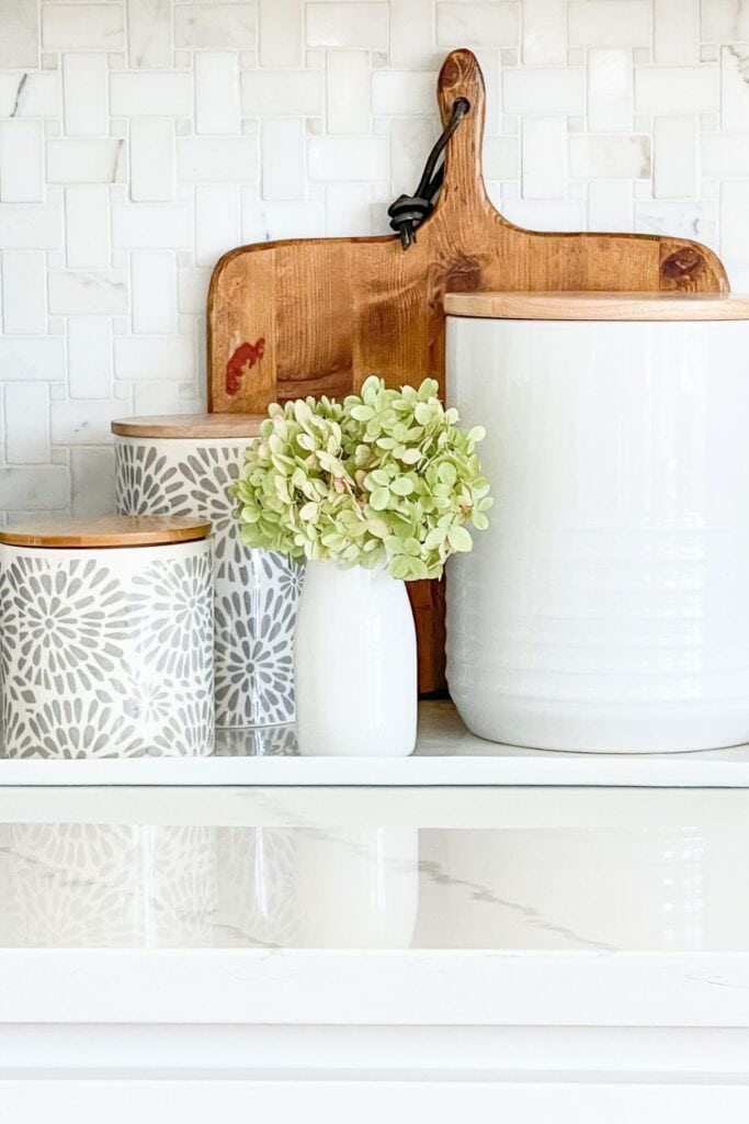 white kitchen canisters with wood lids styled on an organized kitchen countertop with cutting board and hydrangea