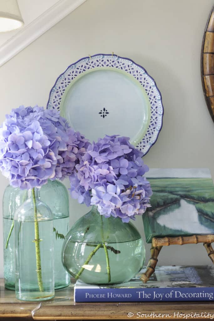cut blue hydrangeas in an aqua glass jugs.