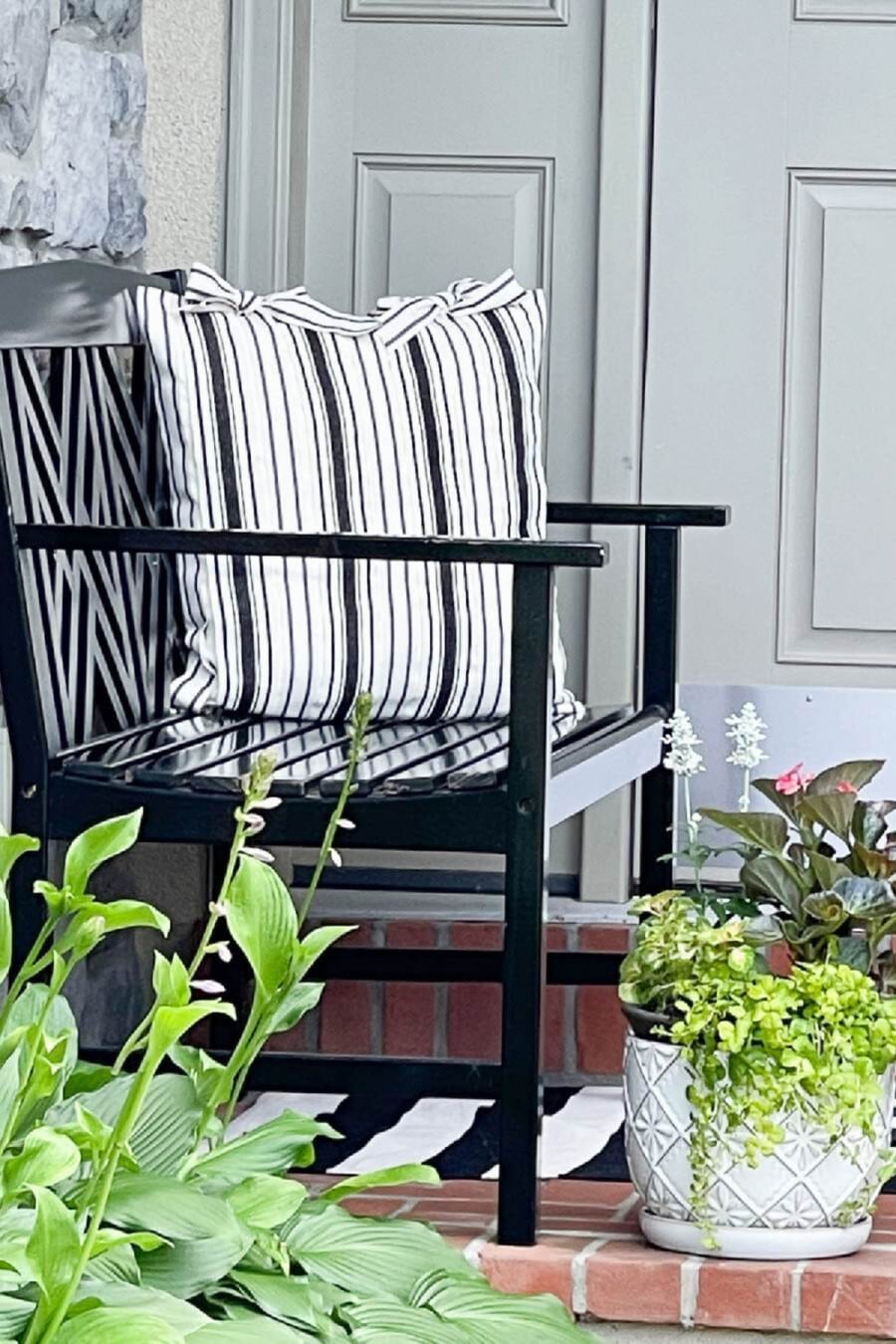 black bench on a front porch with potted flowers
