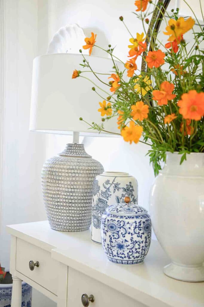 orange flowers in a white vase on a console table