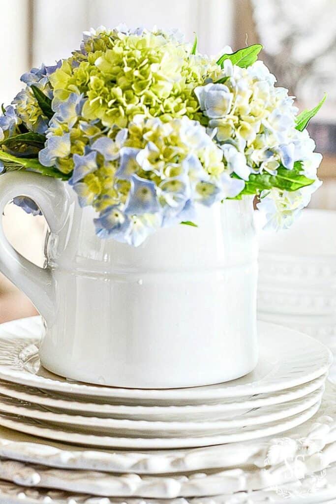 blue hydrangeas in a white pitcher on a stack of plates