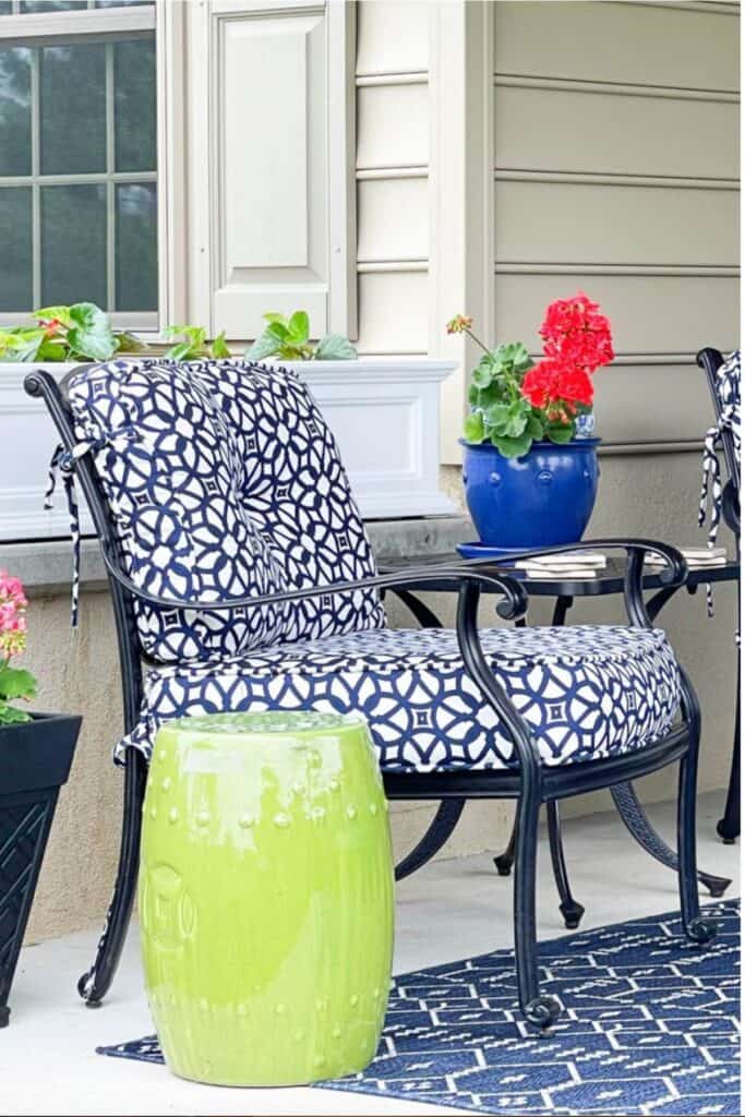 cast iron patio chairs with navy blue and white patterned cushions, lime green garden stool, and potted red geranium on a summer patio