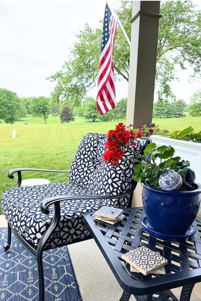 covered patio with navy blue and white patterned chair cushions, potted red geranium, American flag, and golf course view