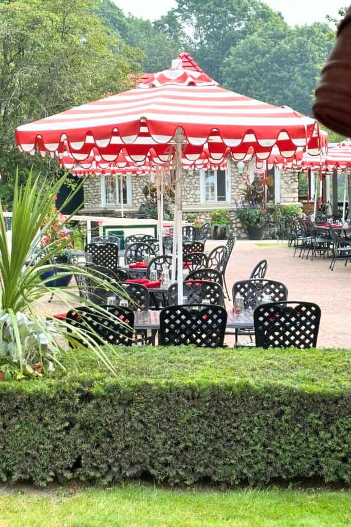 outdoor dining area with black cast iron chairs and red and white striped patio umbrellas surrounded by lush greenery