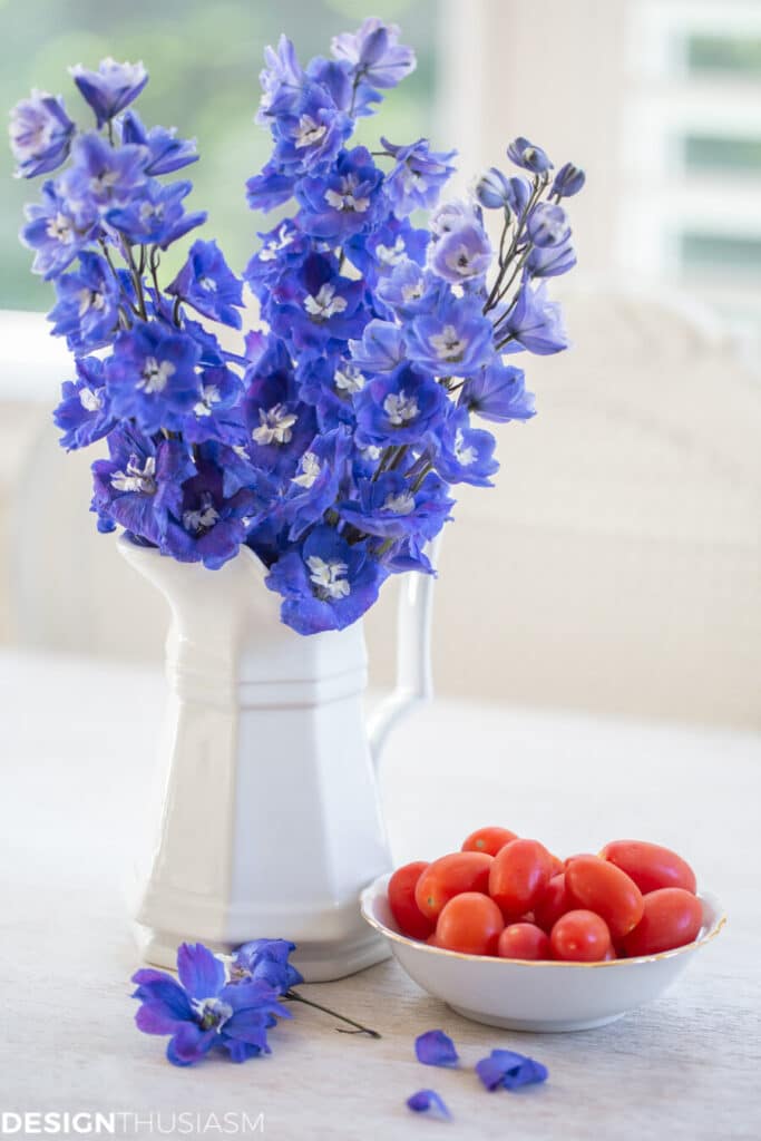 vase of purple flowers next to a bowl of tomatoes