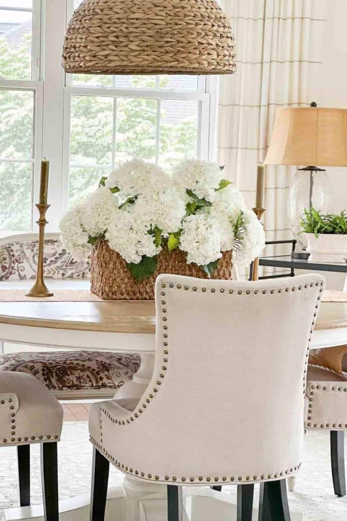 simple dining table centerpiece with white hydrangeas in a basket and candles on a round table