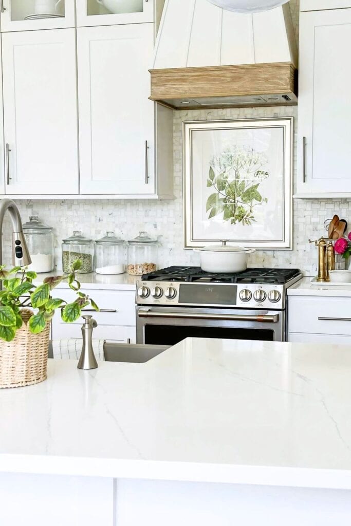 simple kitchen ideas showing clean countertops with glass canisters, greenery, and styled stove area in a white kitchen