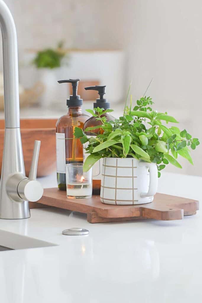 simple kitchen ideas styling a sink area with a wooden tray, fresh herbs, amber bottles, and a candle on a white countertop