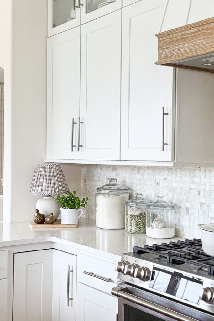 simple kitchen ideas styling a countertop with glass canisters, a small lamp, and greenery in a white kitchen