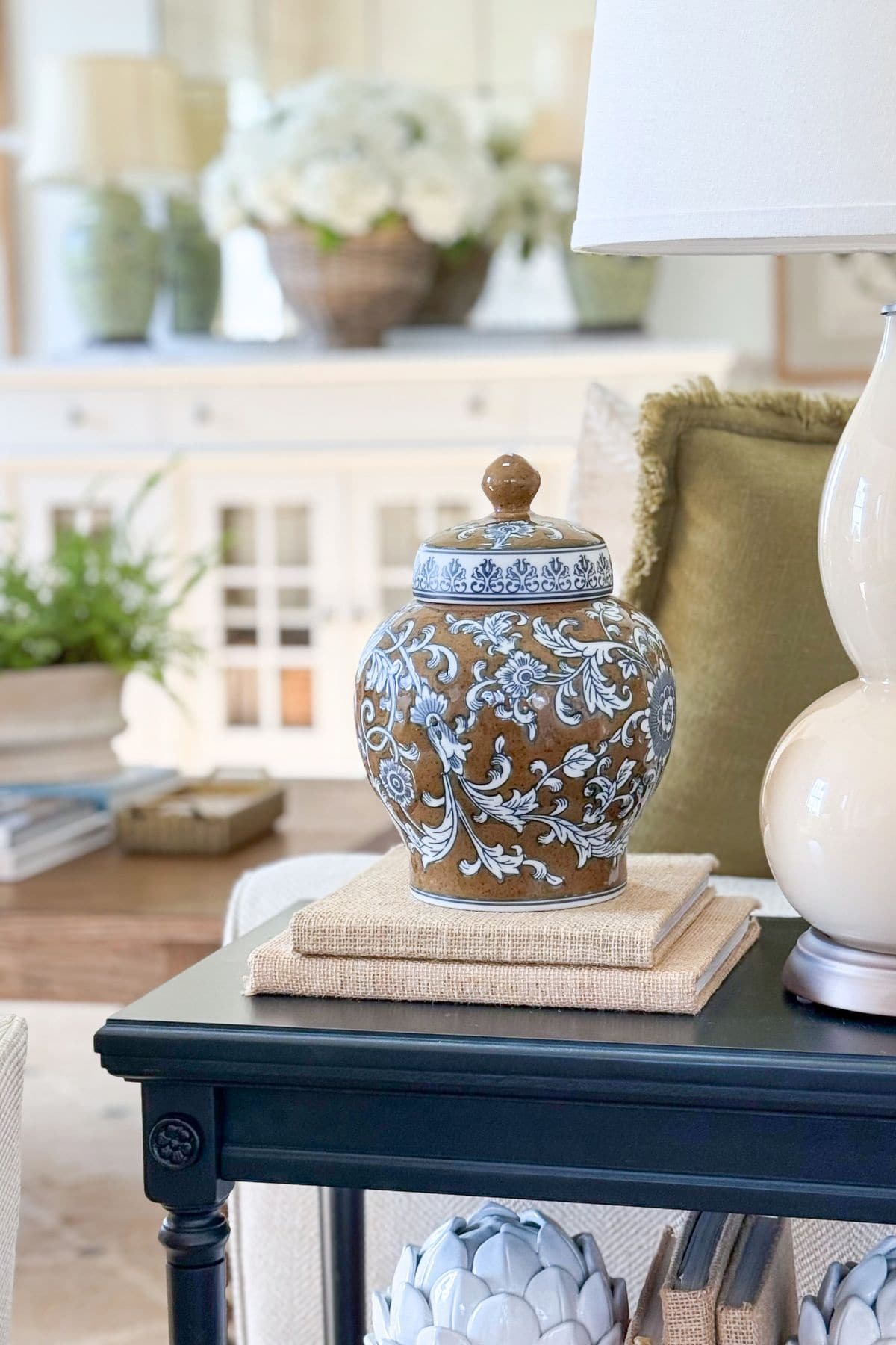a brown, blue and white ginger jar on a stack of books on a living room end table. A layered, cohesive detail.