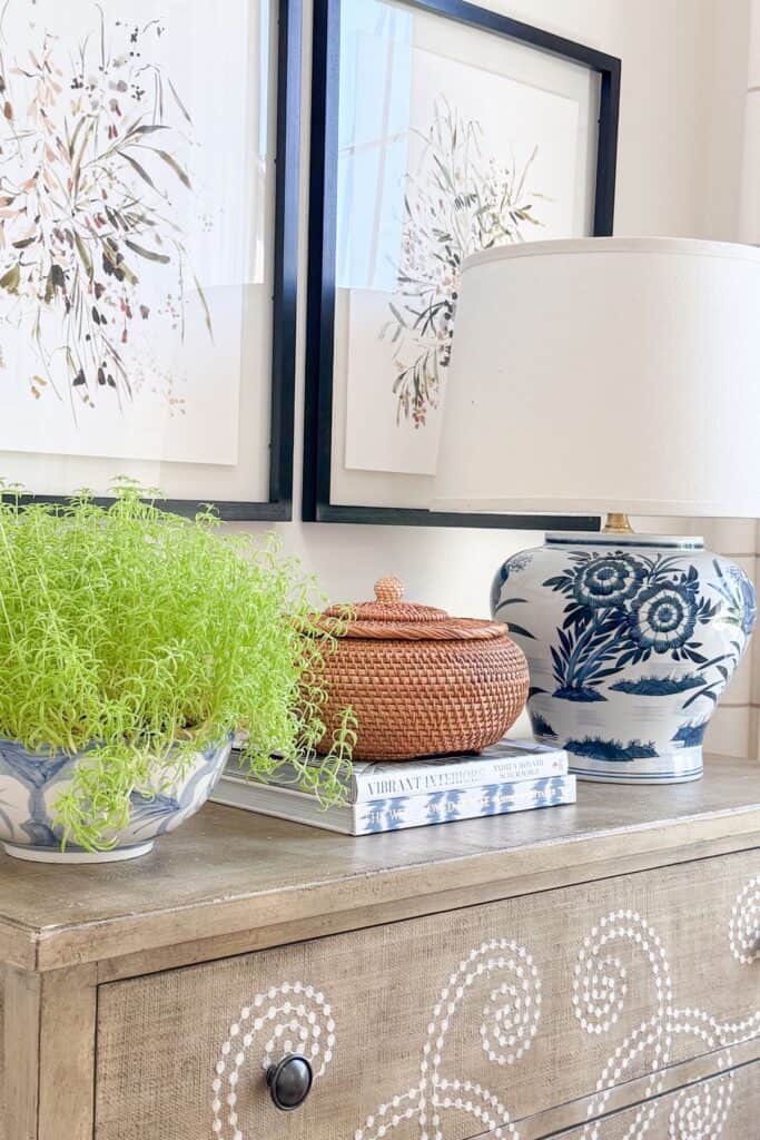 Blue and white bowl with trailing greenery styled beside a woven basket and stack of books on a wood dresser