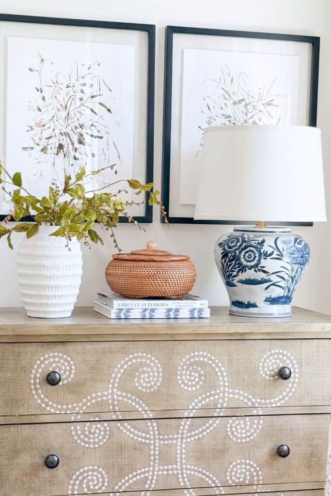 Woven rattan basket and stack of design books styled next to a blue and white chinoiserie lamp on a wood dresser