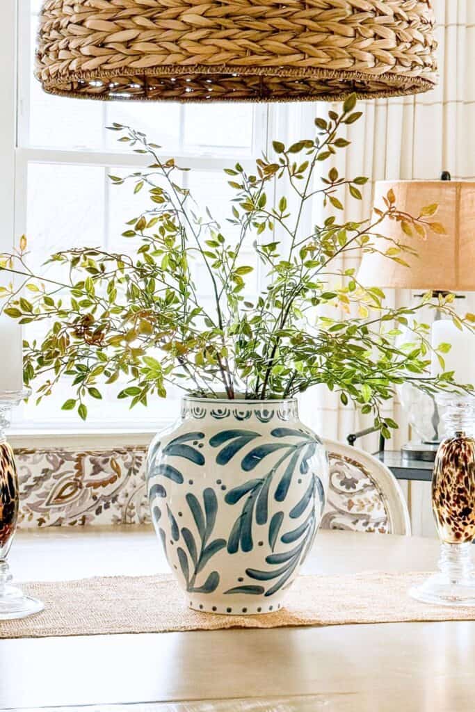 A blue and white ceramic vase filled with fresh green branches styled as a dining table centerpiece at Tanglewood House, showing how to bring the outdoors in to decorate with what you have.