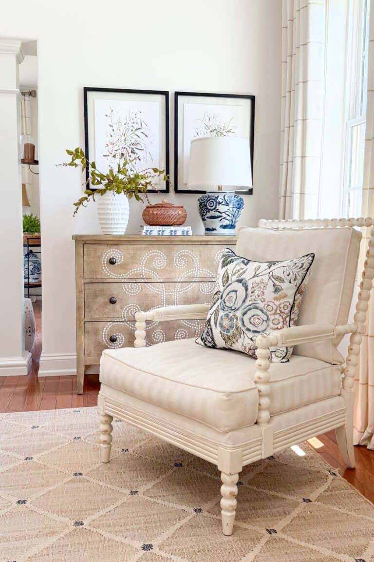 Cream spool chair with floral pillow in front of a wood dresser styled with a blue and white chinoiserie lamp