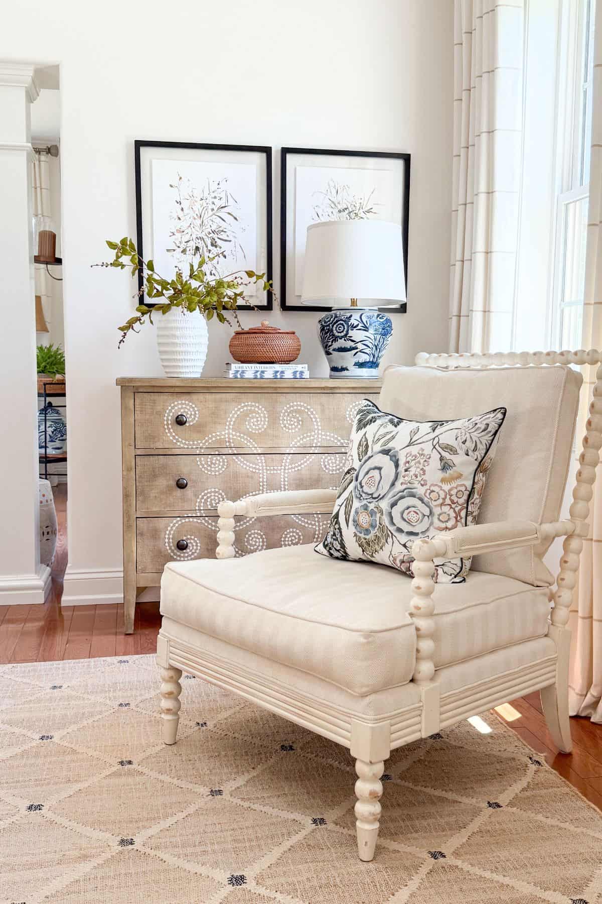 Cream spool chair with floral pillow in front of a wood dresser styled with a blue and white chinoiserie lamp