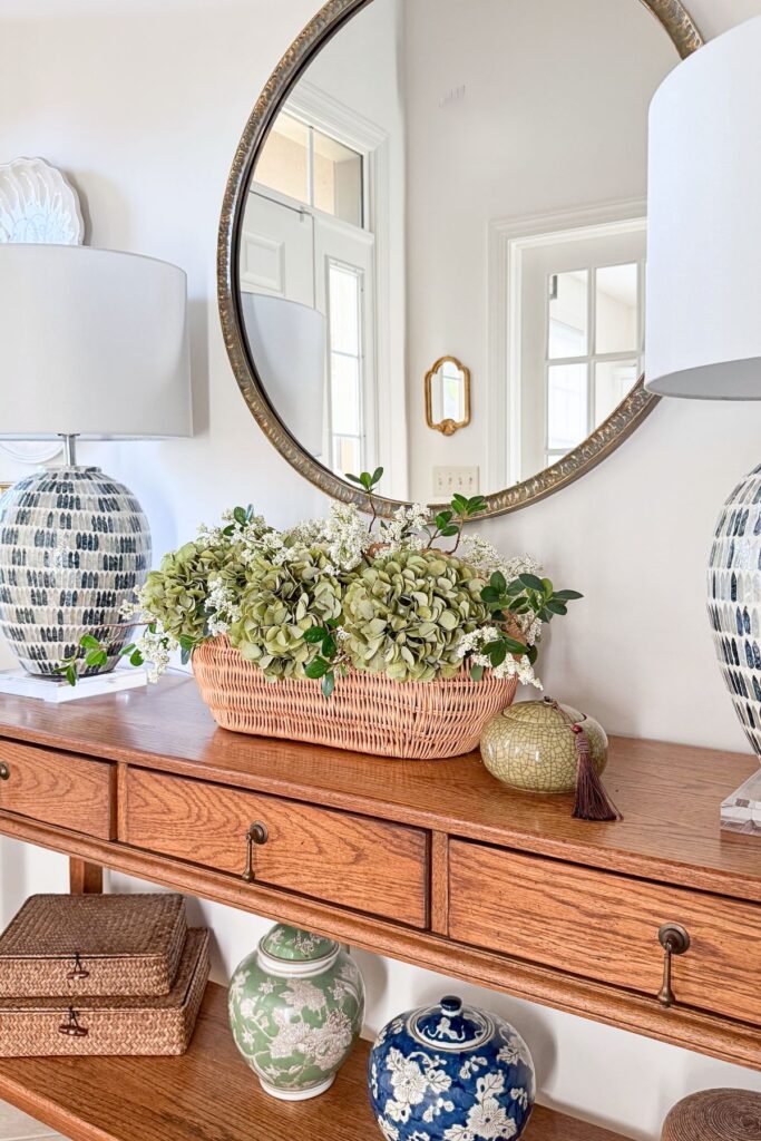 Entryway console table with a drawer, lamp, and woven bag on a hook