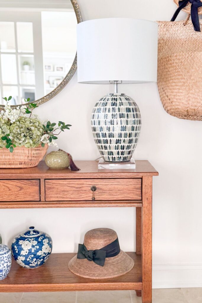 Entryway console table with a drawer, lamp, and woven bag on a hook
