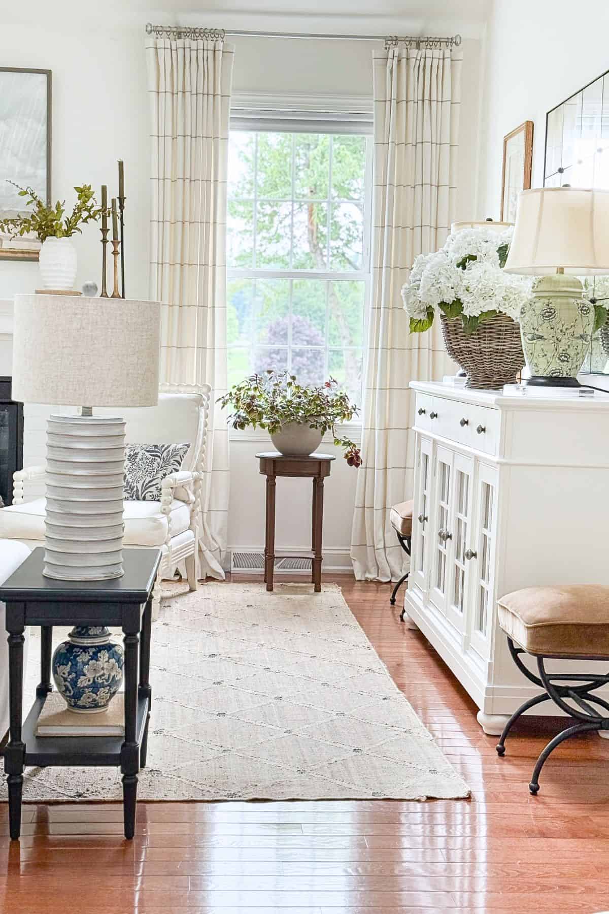 Neutral living room at Tanglewood House styled with a ginger jar, white hydrangeas in a basket, layered rugs, and a large white table lamp showing how to decorate with what you have.