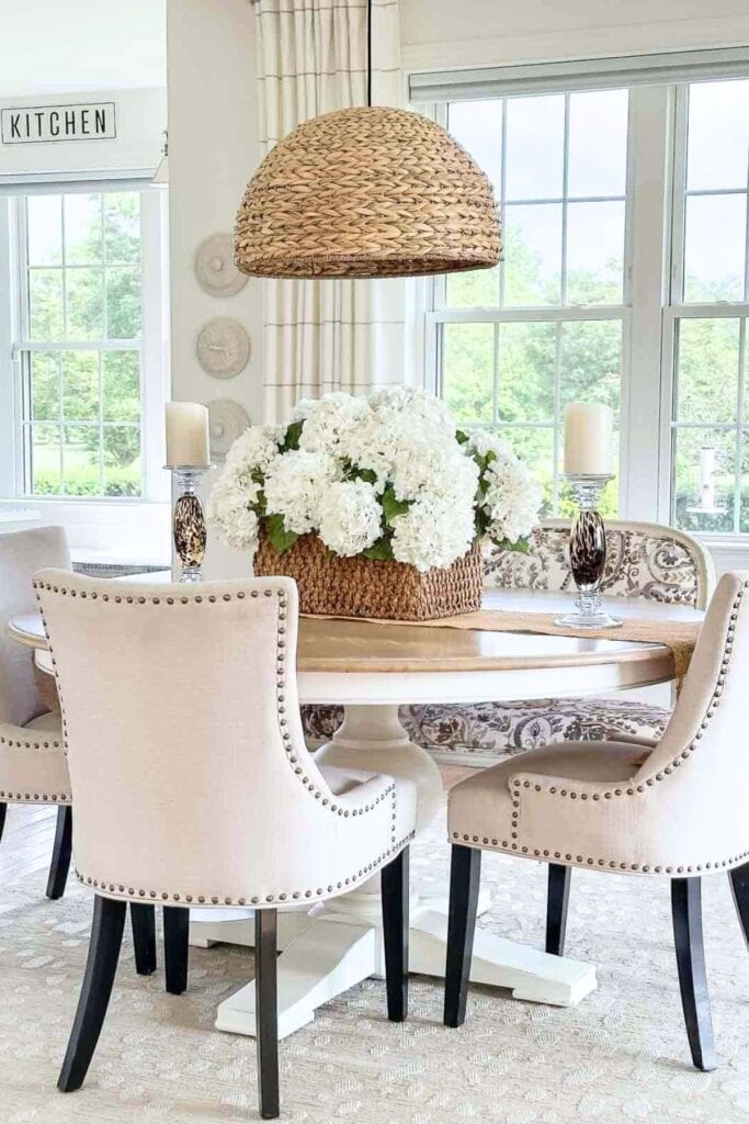 A dining room with a hydrangea centerpiece, neutral chairs and woven pendants showcases a cohesive home design.