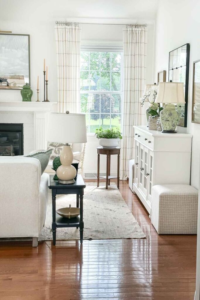 bright neutral living room with white sofa, floor length curtains hung near the ceiling, chinoiserie lamps, and green accents on a white buffet