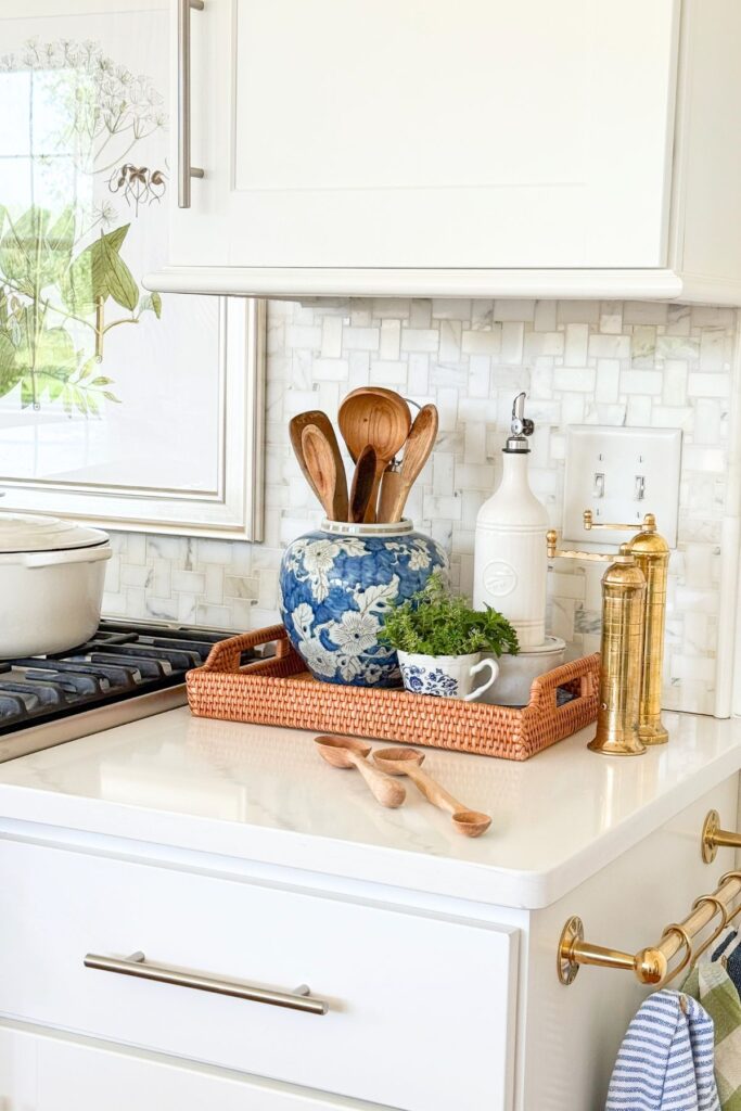 Woven tray corralling wooden utensils, olive oil, and herbs on a small kitchen counter