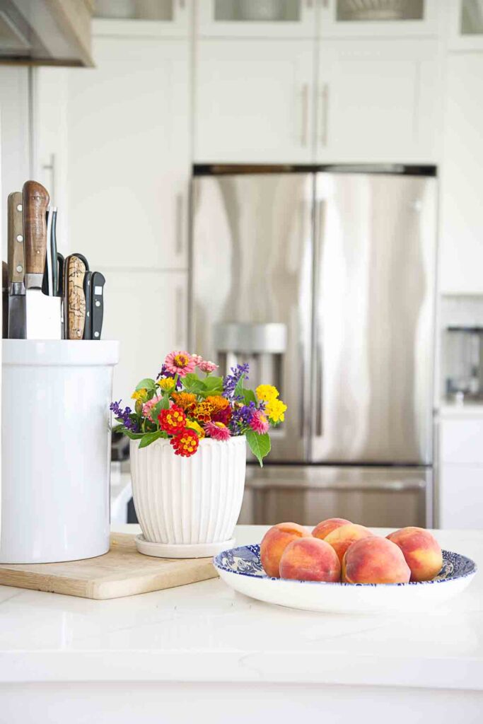 plate of peaches and ceramic pot of garden flowers on a kitchen counter
