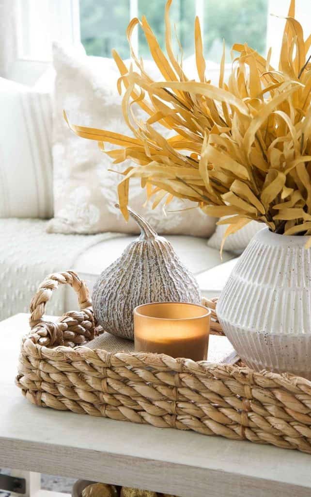 Fall vignette on a coffee table with golden fall stems in a white ribbed vase, a gray gourd, and an amber candle on a woven tray