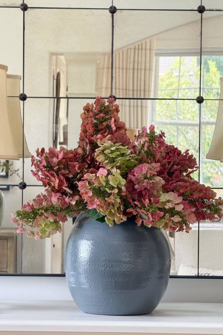 Dried pink and green hydrangeas in a gray ceramic vase styled in front of a mirror