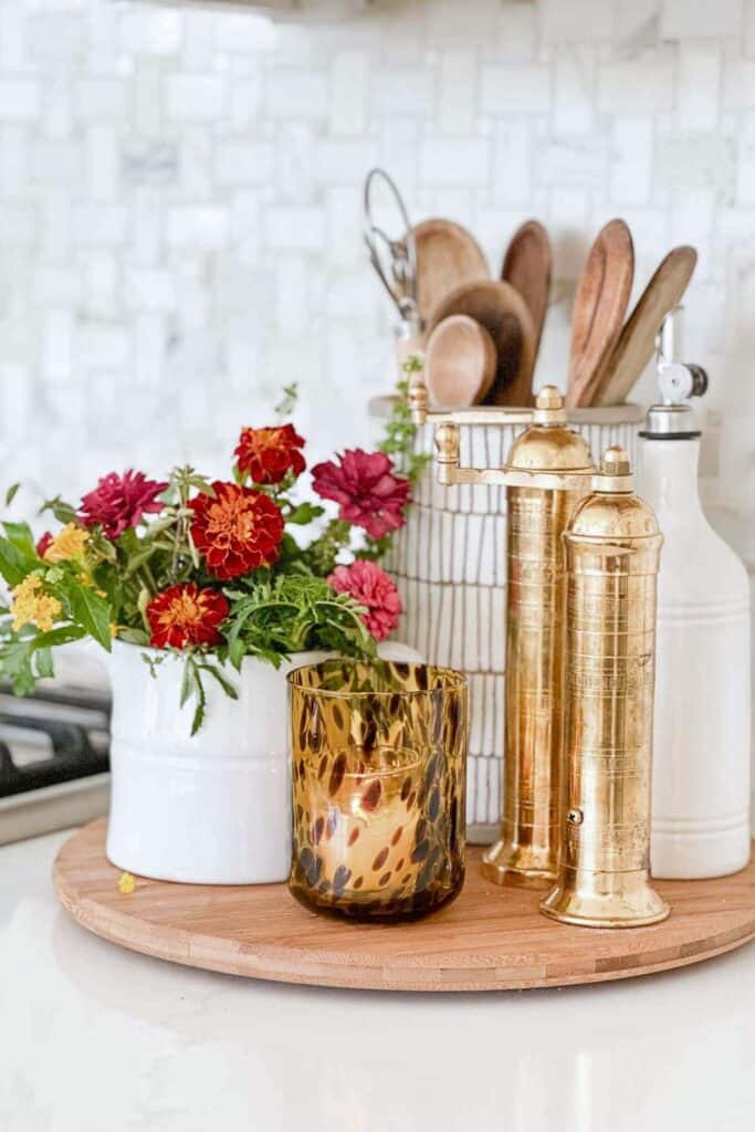 Fall kitchen centerpiece with marigolds, brass pepper mills, and wooden utensils on a lazy susan