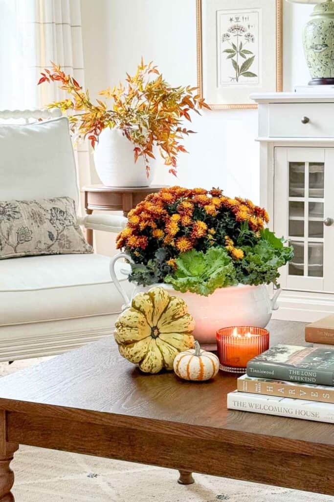 Rust colored mums and ornamental cabbage in a white tureen styled on a coffee table for fall