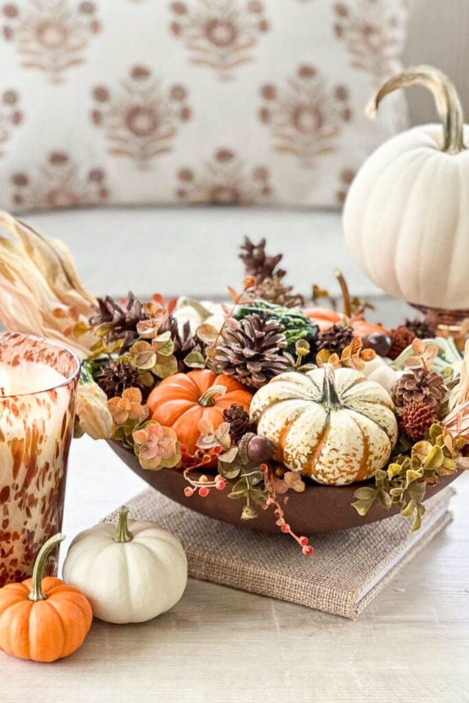 Budget friendly fall decorating with real and faux pumpkins, pinecones, and dried florals in a wooden dough bowl centerpiece.