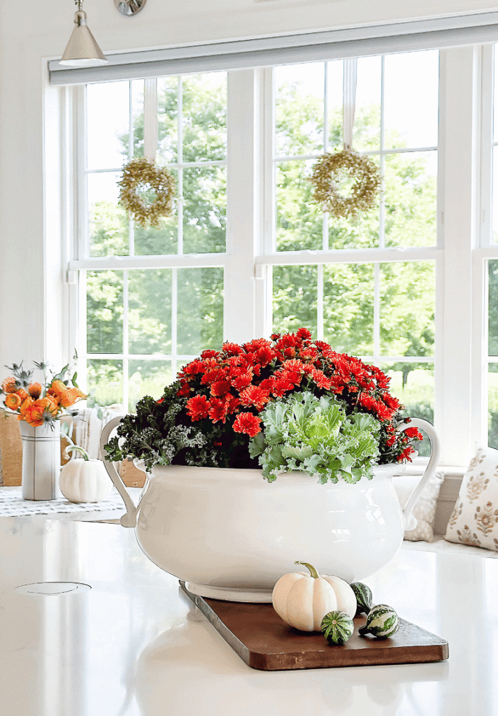 White soup tureen filled with orange mums and ornamental cabbage on a fall table