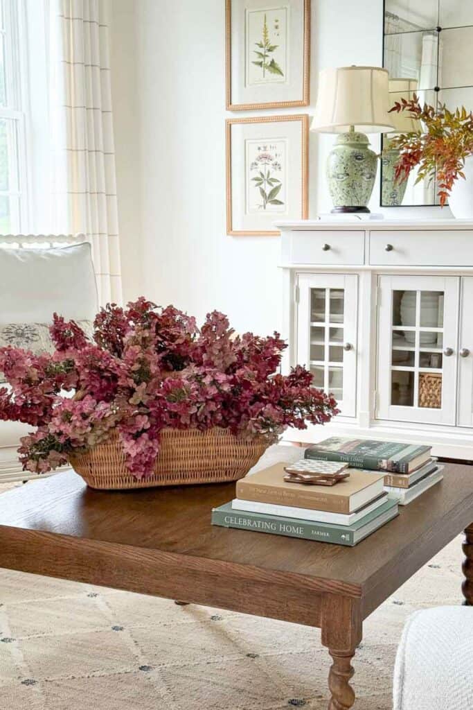 Fall living room decor with a basket of hydrangeas on a wooden coffee table, layered books, and simple seasonal accents.