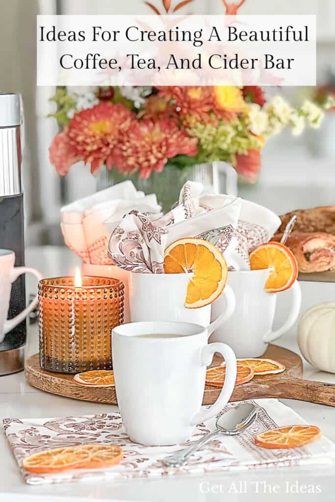 Fall coffee, tea, and cider bar styled with white mugs, dried orange slices, fall flowers, and a lit candle.