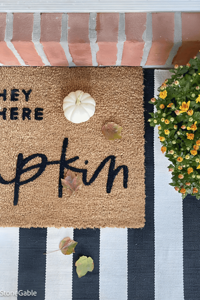 Pumpkin doormat layered over striped rug on a fall porch