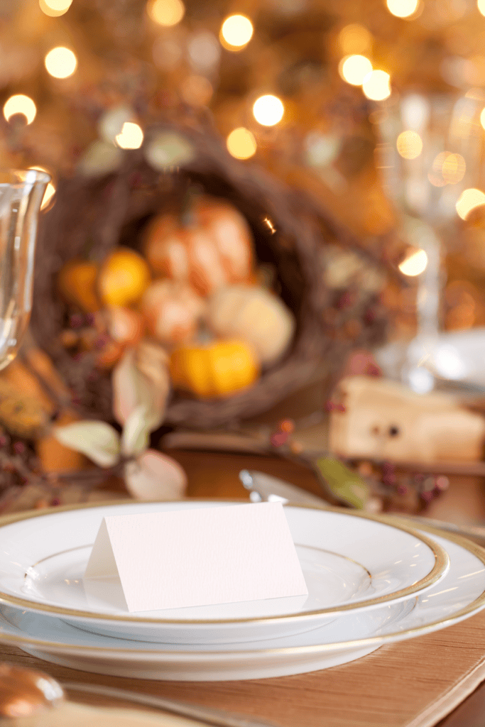 a white Thanksgiving place setting with a cornucopia in the background 